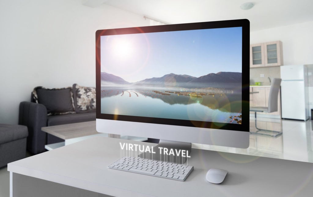 large-computer-monitor-on-desk-in-home-office-displaying-scenic-lake-and-mountains-with-the-words-virtual-travel-under-screen